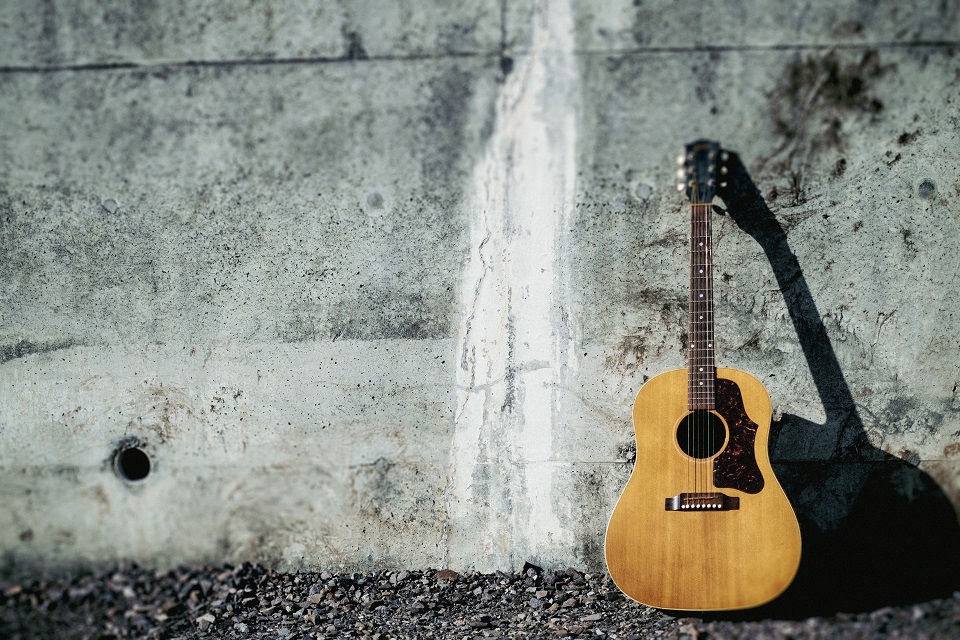 コンクリートの壁に立てかけられたアコースティックギター